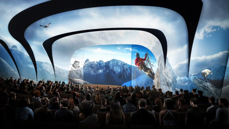 The audience is watching a real show in a theater with curved, futuristic screens that show the beauty of the mountains, the rider, the eagle and the bear, which makes for a spectacular and captivating sight.