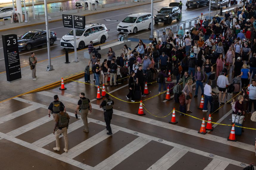 Immigration and Customs Enforcement officials walk by as travelers line up outside Terminal E at George Bush Intercontinental Airport on Friday in Houston, Texas.
