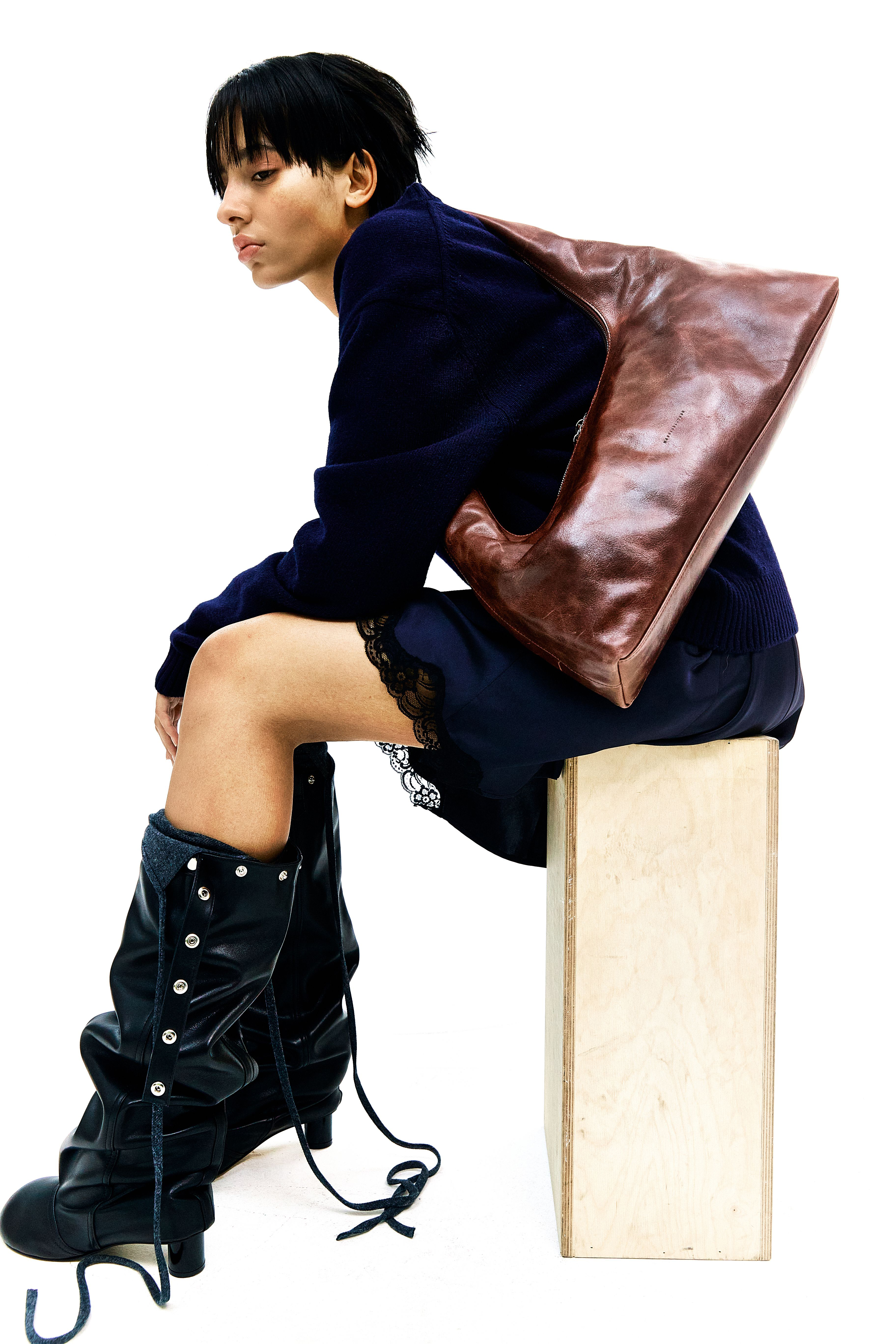 a woman wearing a brown shoulder bag, a black dress, and black boots