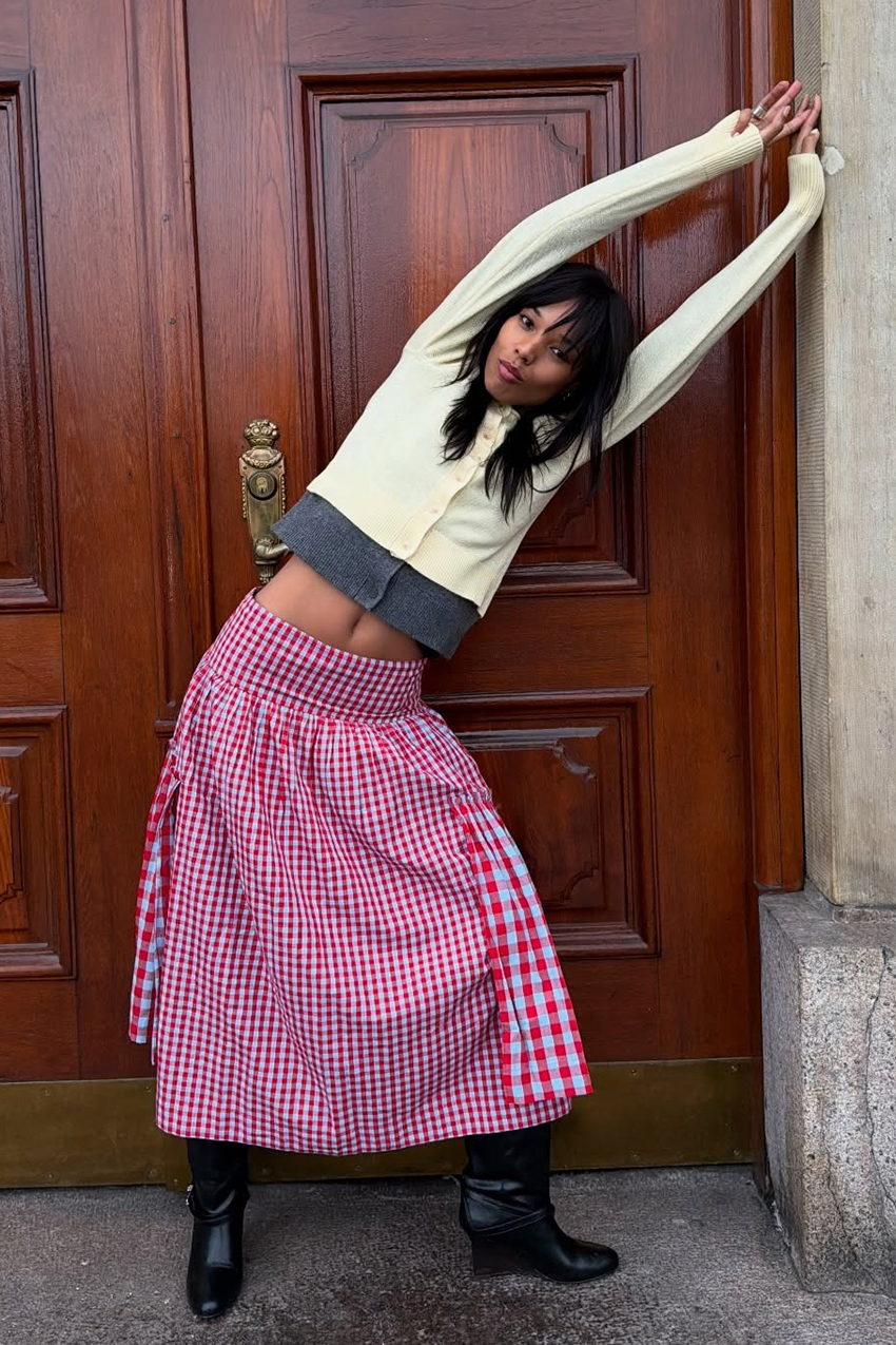 a woman wearing a buttery yellow cardigan, a red gingham skirt, and black shoes
