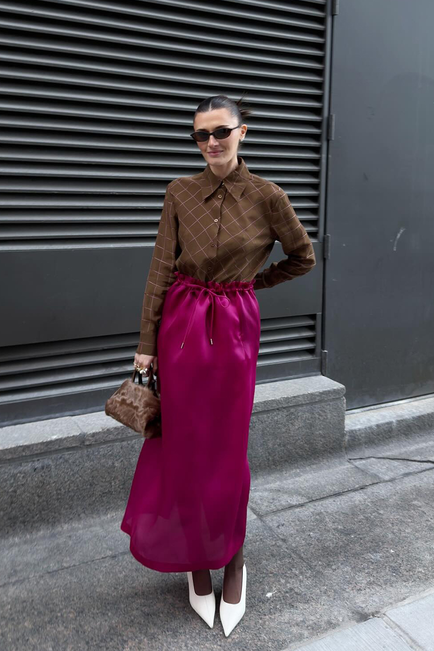 A woman wearing brown buttons, a pink dress, and white pointed toe shoes.