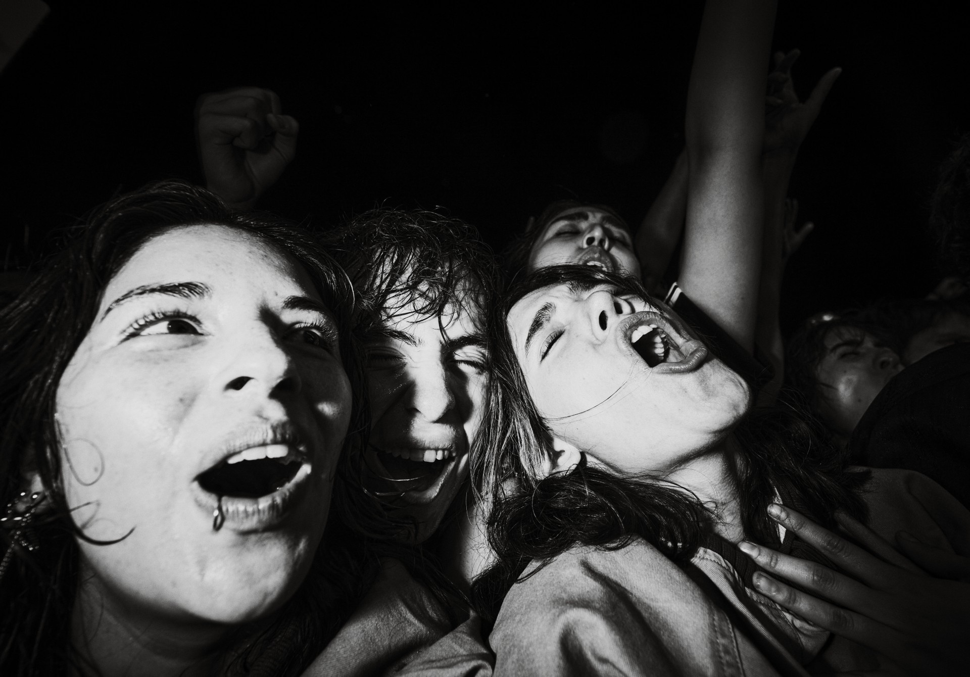 A powerful, close-up black-and-white photograph captures the emotion and excitement of several screaming fans in the front row of a concert.