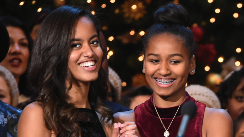 Malia Obama smiles next to Sasha Obama behind the microphone