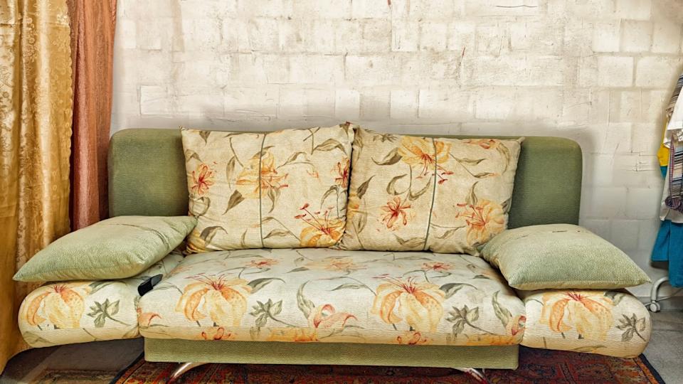 A floral sofa in soft green and beige colors is placed against a patterned wall, surrounded by warm curtains and a sophisticated rug.