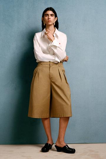 a woman wearing a white button down, beige shorts and black shoes