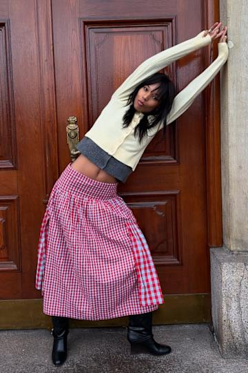 a woman wearing a buttery yellow cardigan, a red gingham skirt, and black shoes