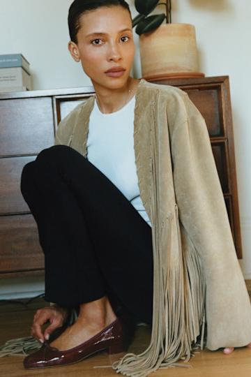 A woman wearing a blazer, white tee, black pants, and burgundy shoes.