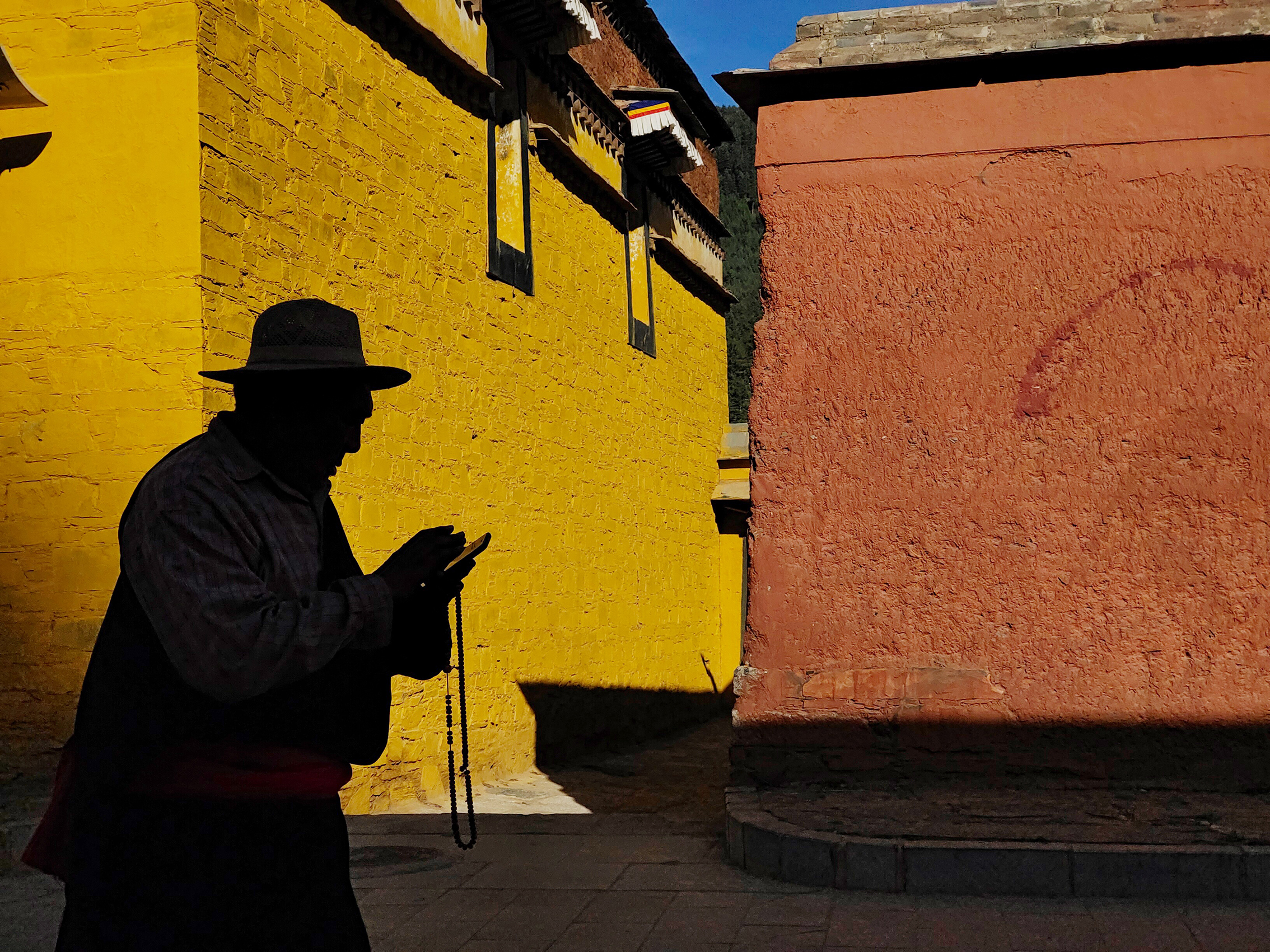 A figure holding prayer beads passes through the bright yellow and orange walls, creating long shadows