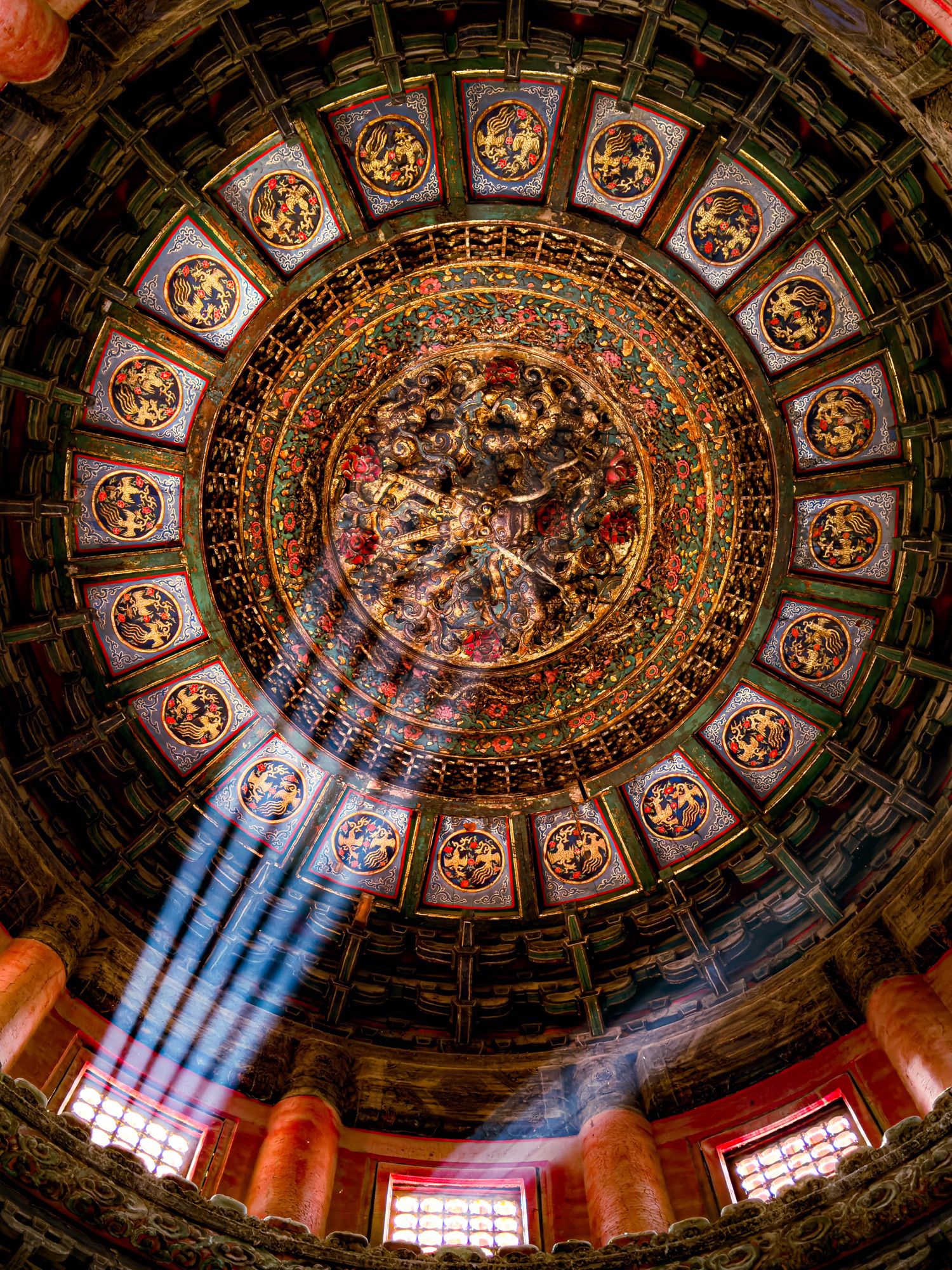 A beautiful circular ceiling with intricate carvings and colorful patterns, lit by sunlight through the windows.