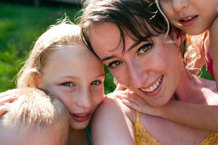 A white woman and three blond children smile for a photo. It's sunny. Some of the children's faces are cut out of the frame.