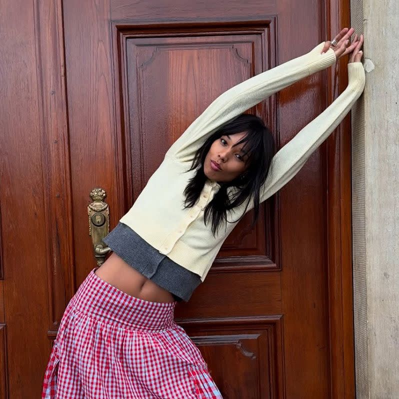 A woman wearing a yellow cardigan and a red gingham skirt.