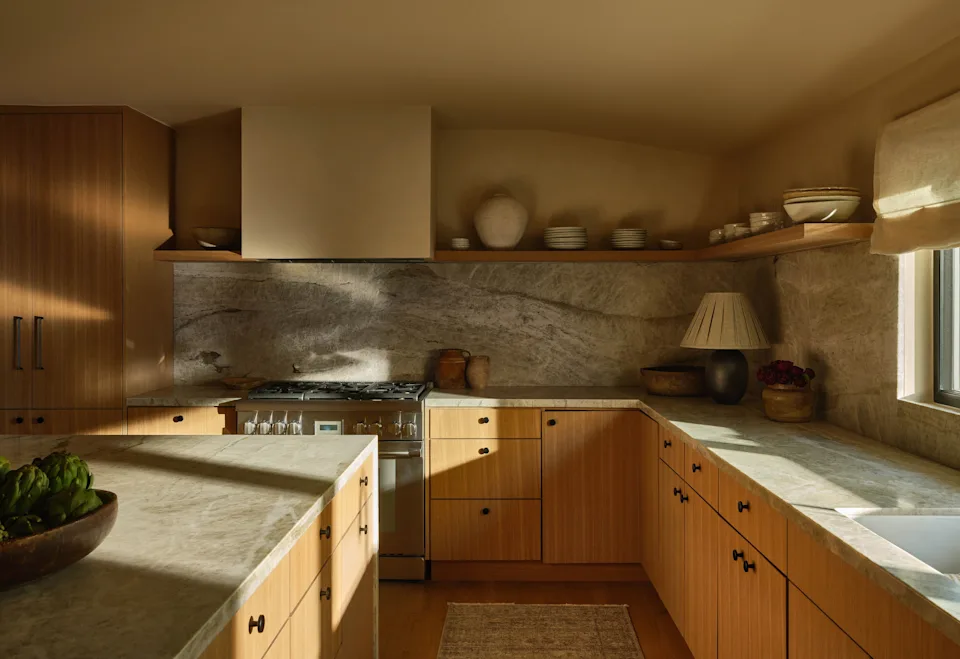 White oak cabinetry, floating shelves, and Taj Mahal stone create a calm palette that extends to the kitchen island, which is upholstered in Teddy chairs by House of Leon. The original counter painting is by Tamasin Reid by Galerie Solis.
