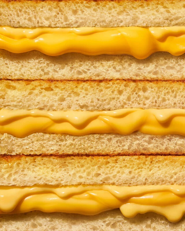 Next to the three grilled cheese sandwiches, it shows golden brown toasted bread and melted yellow cheese flowing between the layers.