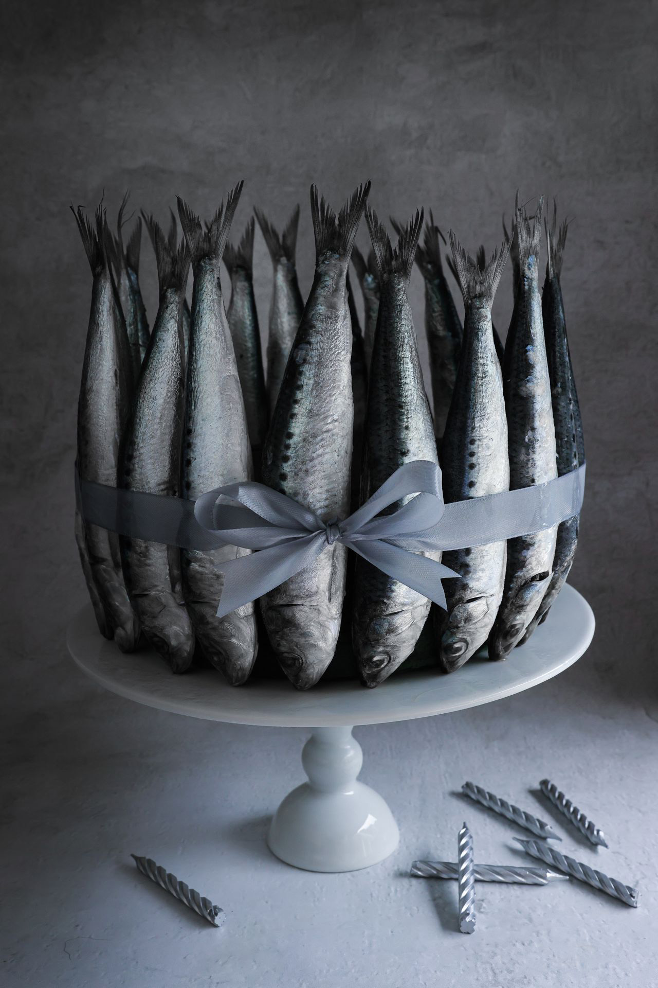 The cake stand features a beautifully designed fish tied with silver ribbon, just like the cake. Gray candles sit nearby