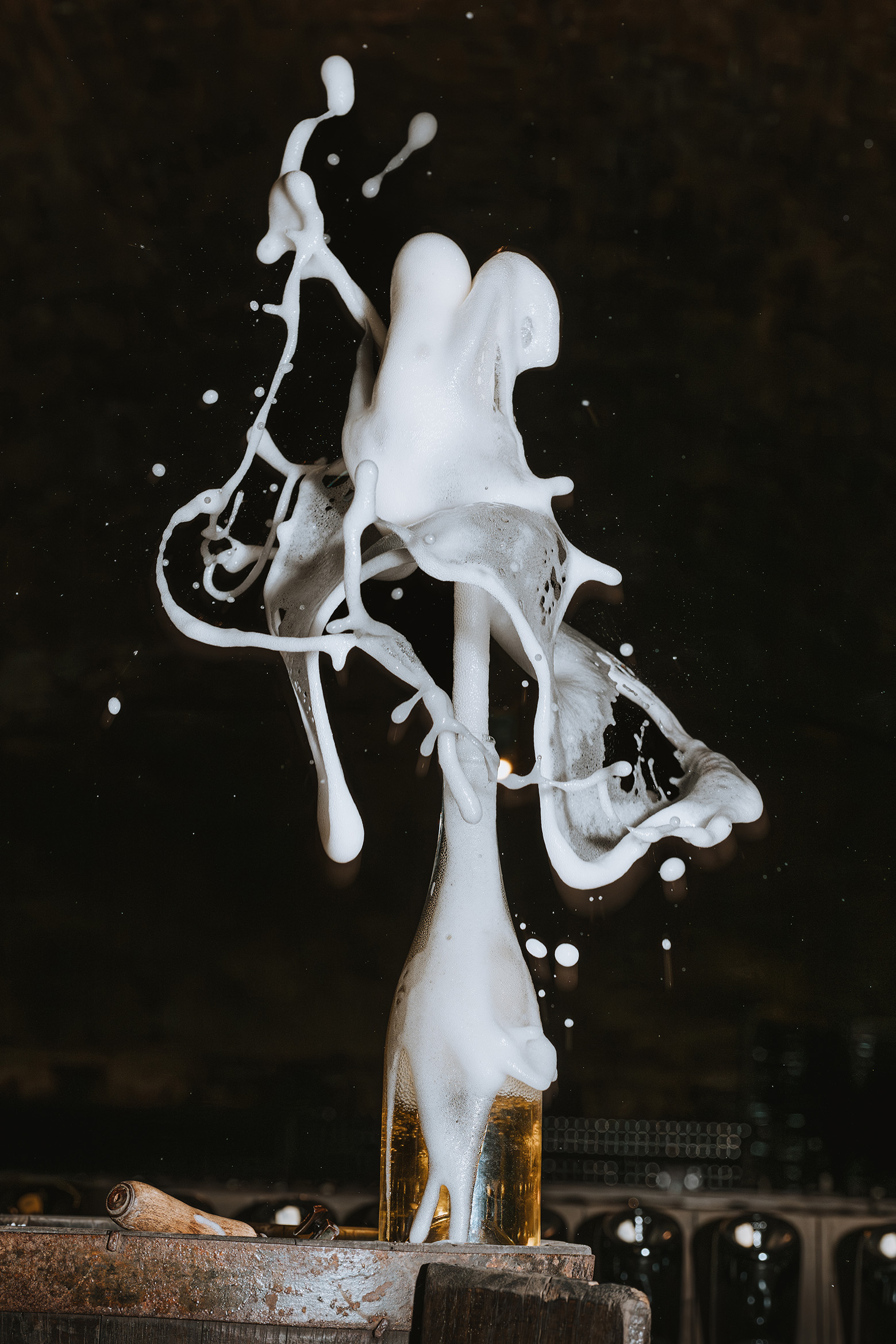 A bottle of Champagne on a wooden barrel explodes with foam, creating strong, circular patterns