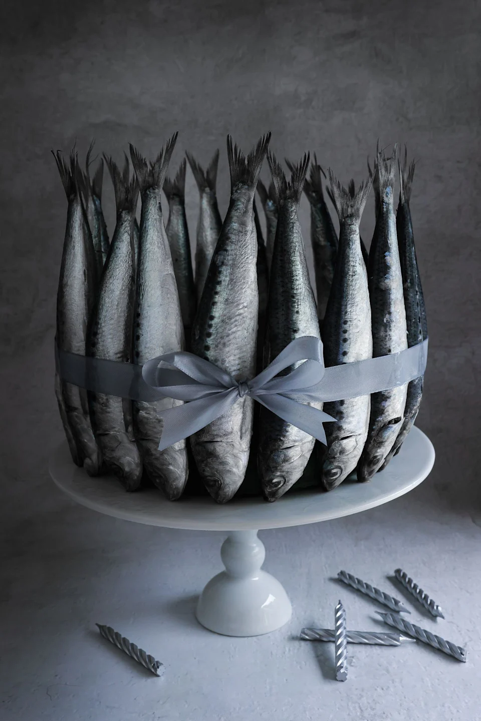 The cake stand features a beautifully designed fish tied with silver ribbon, just like the cake. Gray candles sit nearby