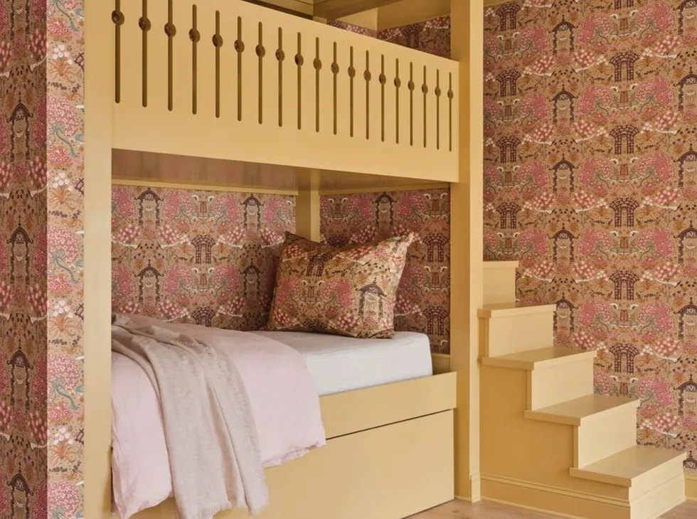 A yellow bed with stairs, floral wallpaper, and pink bedding.