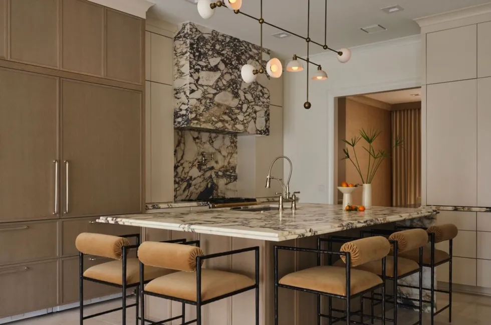 A modern kitchen with marble accents, island seating, and unique pendant lights.