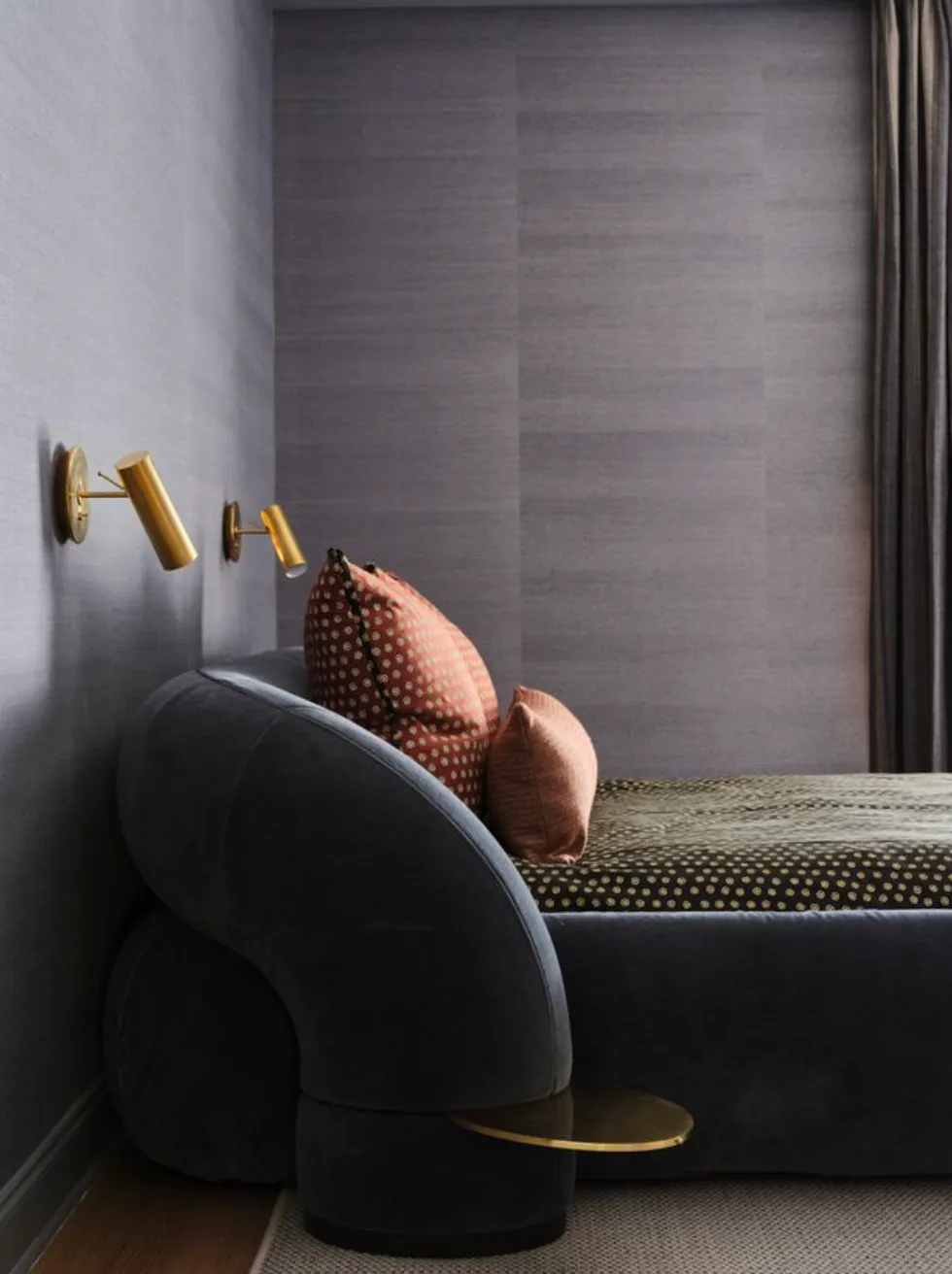 A modern bedroom with a curved bed, polka dot pillows, and copper wall lamps.