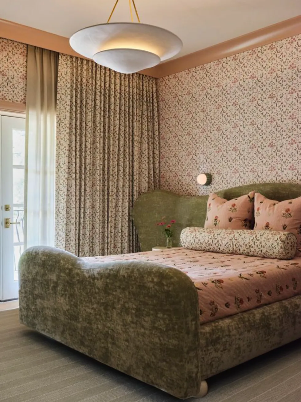 A luxurious bedroom with floral wallpaper, a velvet bed, and a round ceiling light.