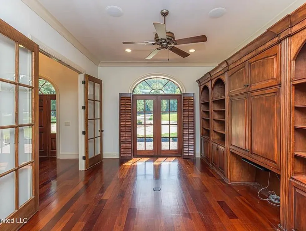 Spacious living room with wooden shelves, French doors, and ceiling fan.