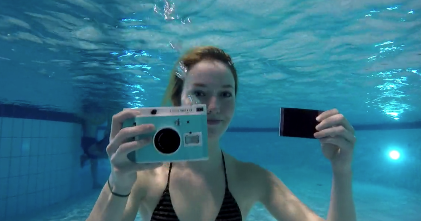 Underwater instant camera is held underwater by a female swimmer